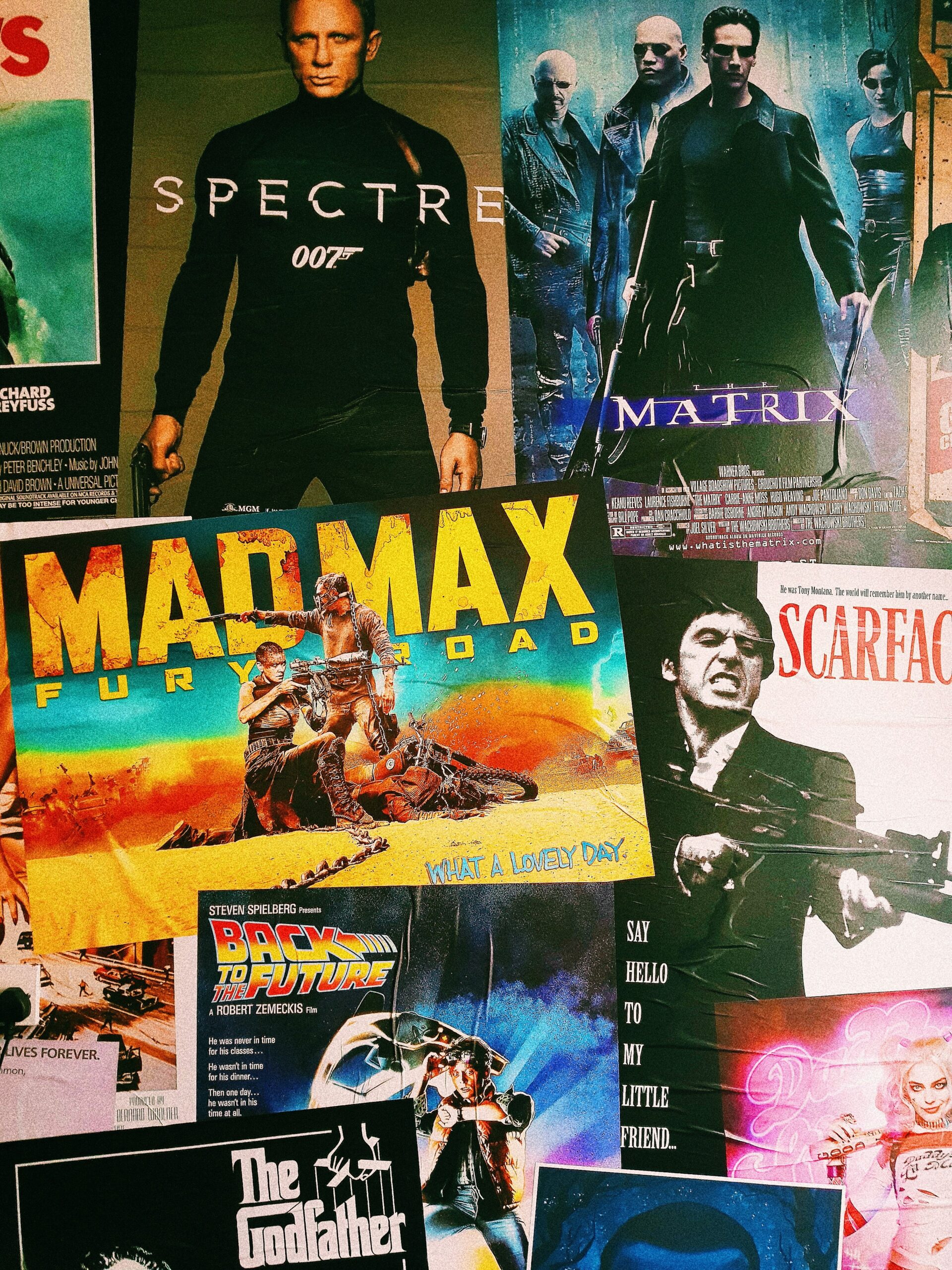 A collage of iconic movie posters including Spectre, The Matrix, Mad Max: Fury Road, Scarface, Back to the Future, and The Godfather, overlapping against a dark background.
